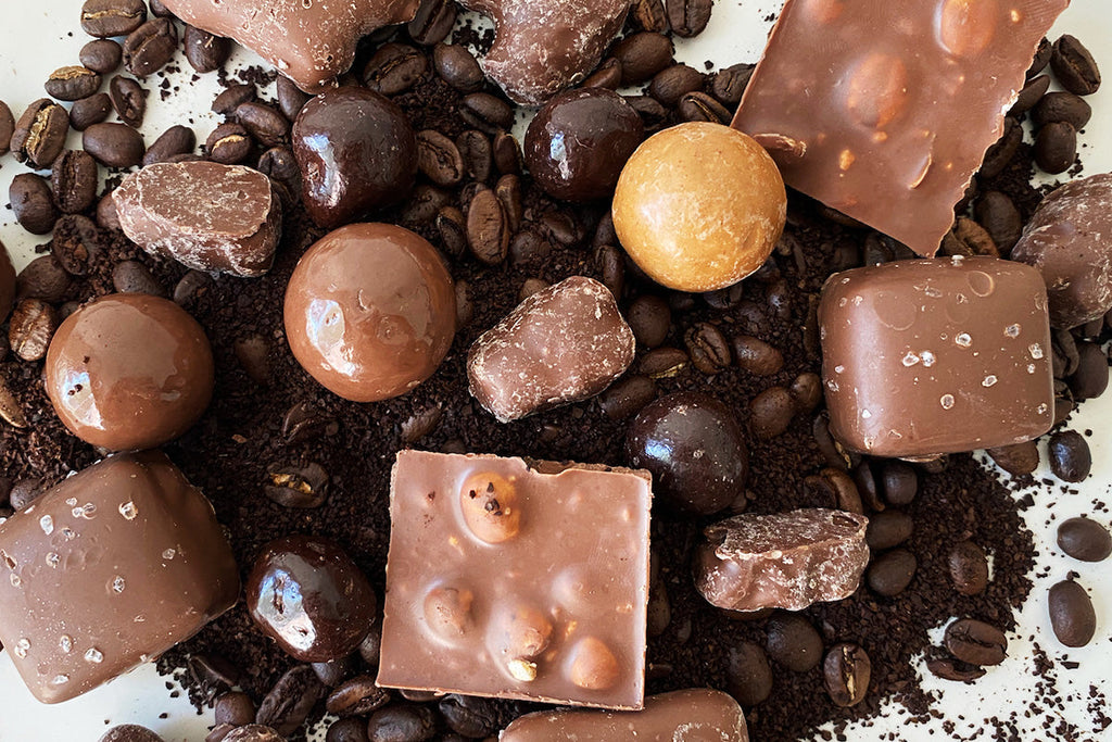 various chocolates sit on top of a pile of whole coffee beans and grounds