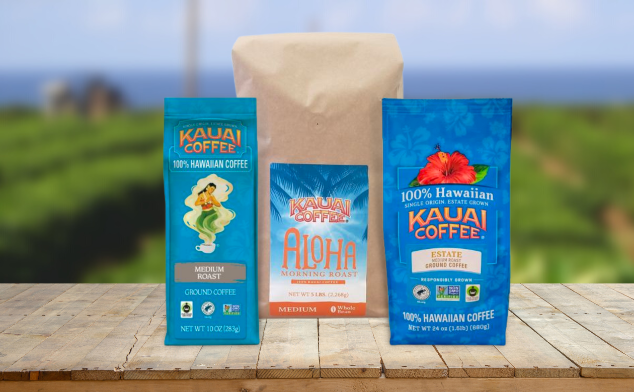 three bags of medium roast 100% hawaiian coffee sit on a wooden surface with a shallow depth of field photo in the background.