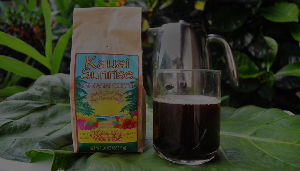 This is an image of a bag of Kauai Sunrise coffee on a table with a cup of coffee and french press, kauai coffee french press, kauai coffee french press